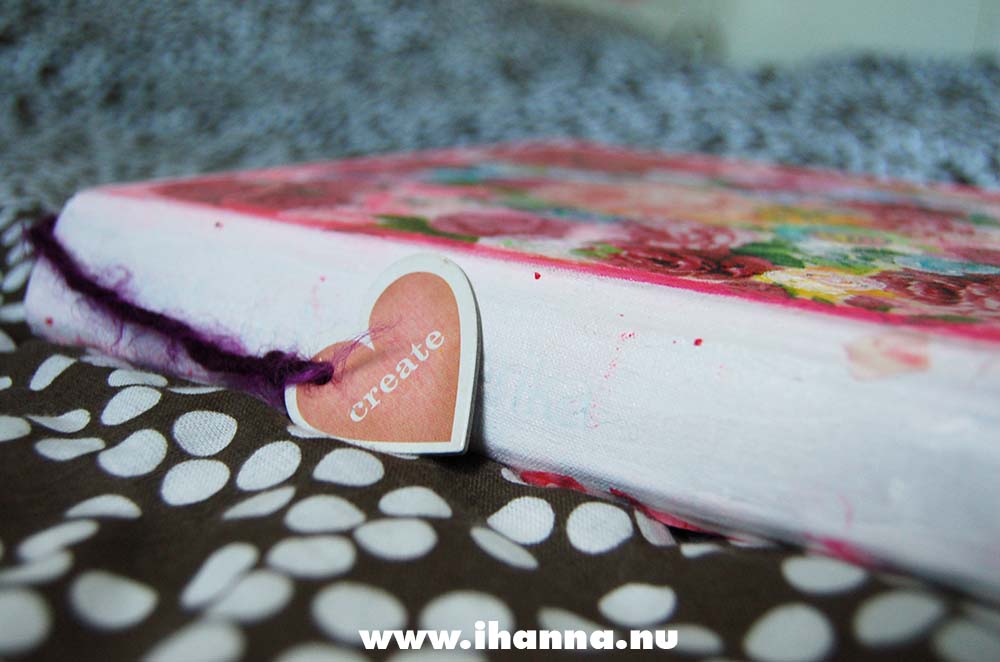 Art Journal spine on the bed with a dangling heart on for art journal inspiration, made by iHanna, Copyright Hanna Andersson