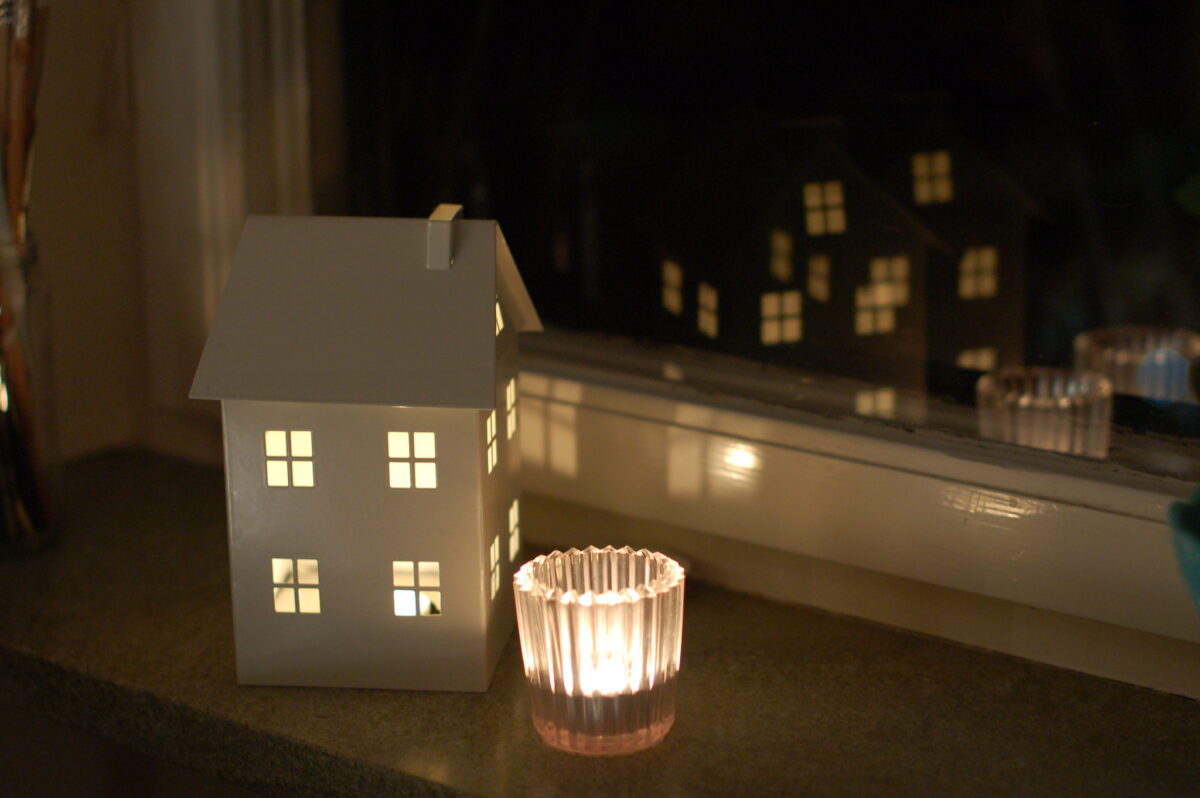 Candle holder that looks like a house reflected in the black winter window. Photo copyright Hanna Andersson
